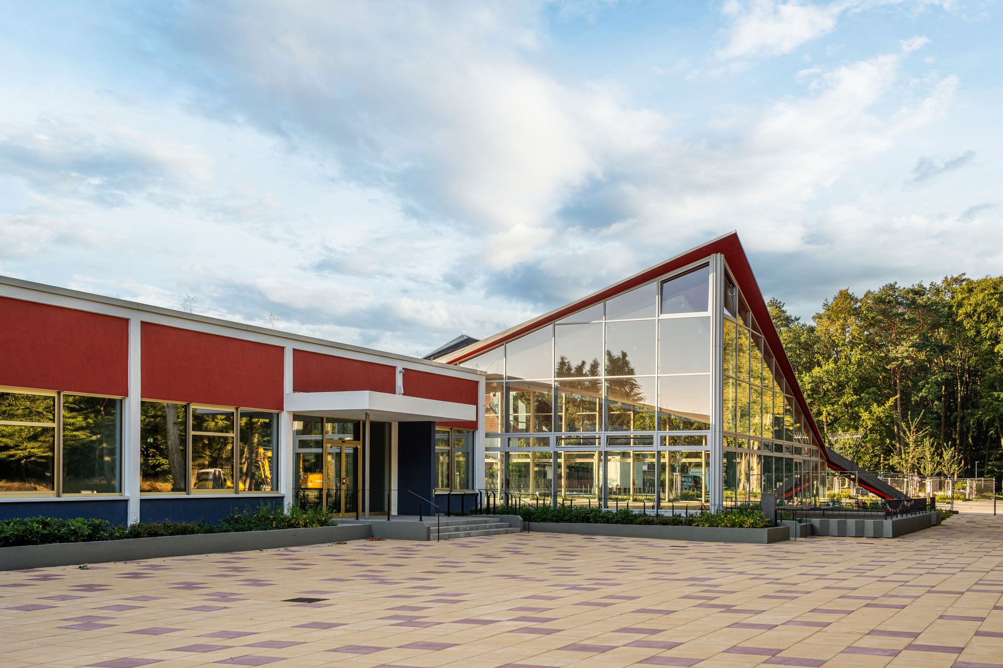A modern public school building with a bright glass facade and an open plaza.